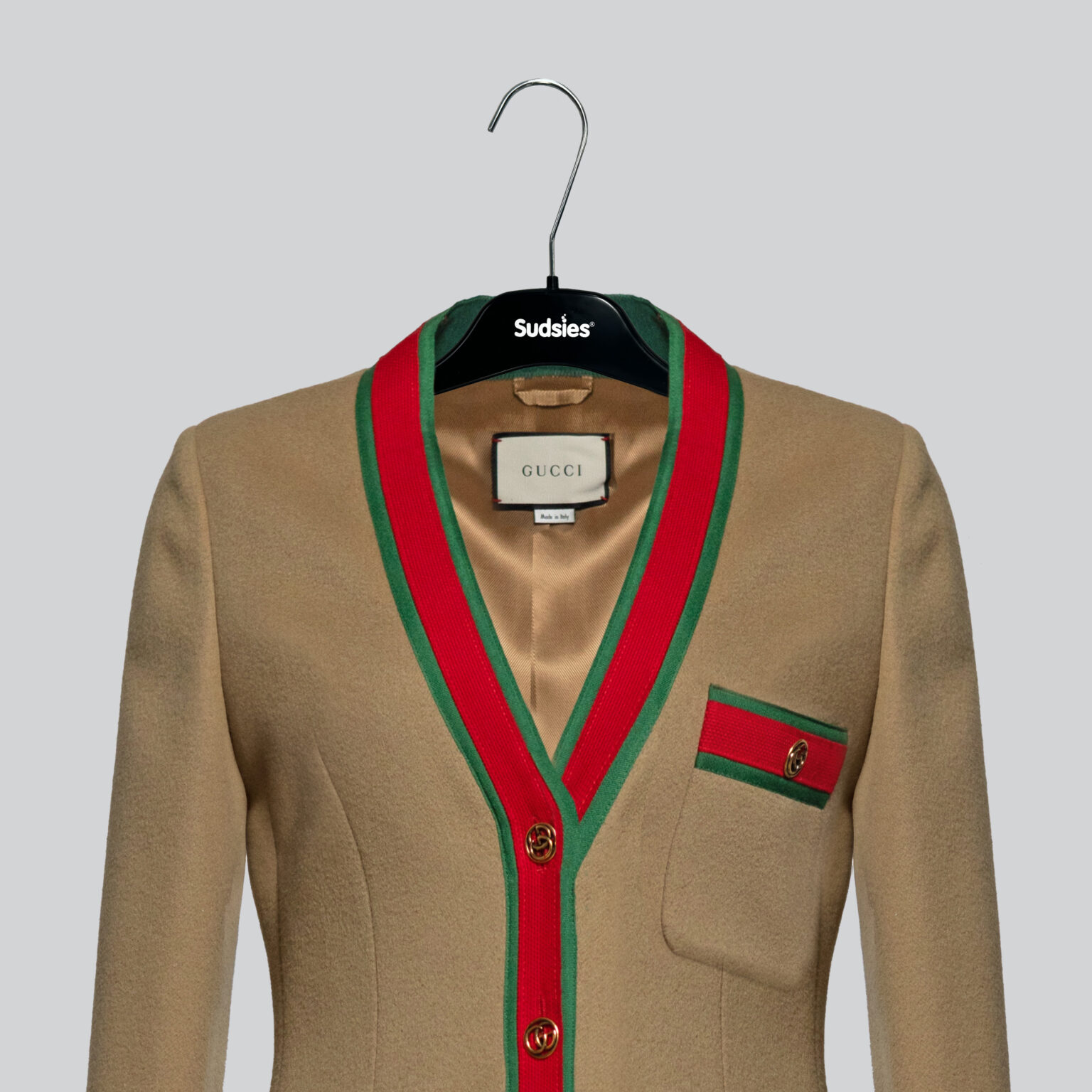 A camel-colored Gucci wool jacket with red and green trim, displayed on a black Sudsies hanger against a gray background.