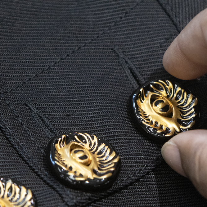 Close-up of a Sudsies technician inspecting a black MAISON SCHIAPARELLI garment with ornate gold-and-black sunburst buttons.
